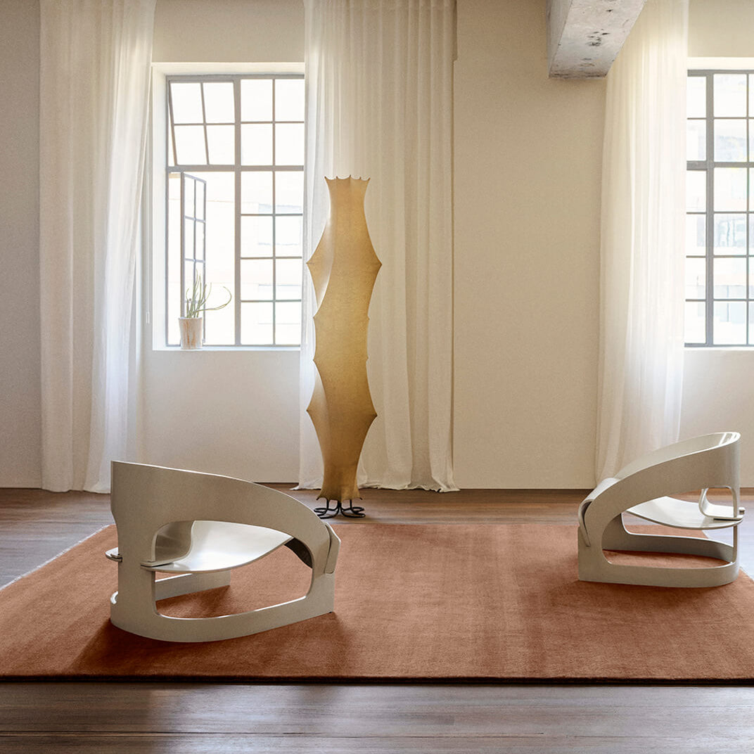 Modern interior with a unique floor lamp and two chairs on a pink rug.