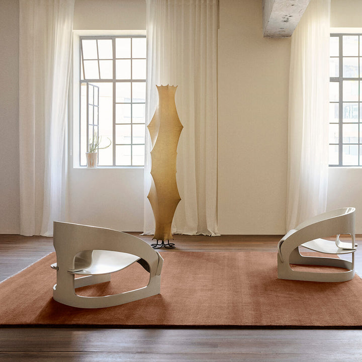 Modern interior with a unique floor lamp and two chairs on a pink rug.