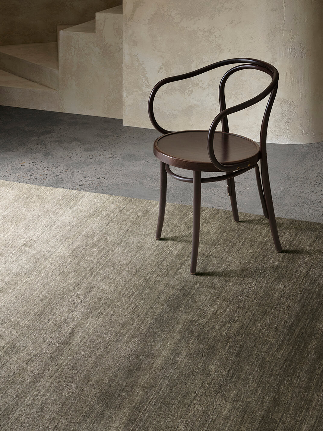 Wooden chair with curved backrest on a textured floor and wall background