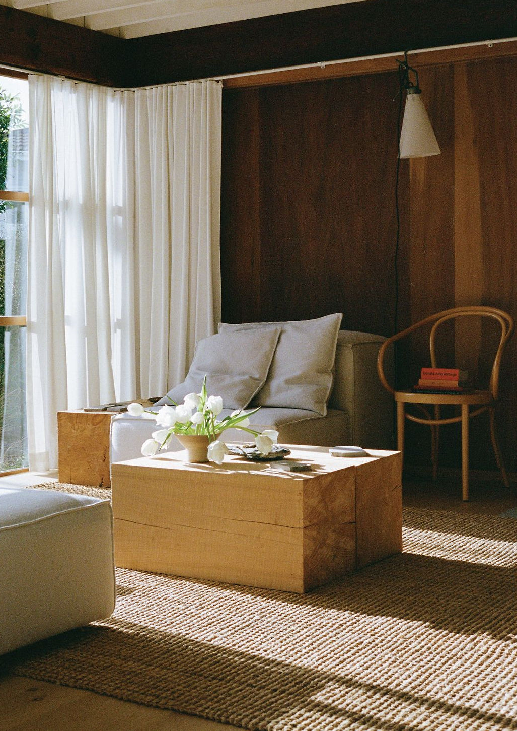 Modern living room with wooden coffee table, white cushions, and large windows.